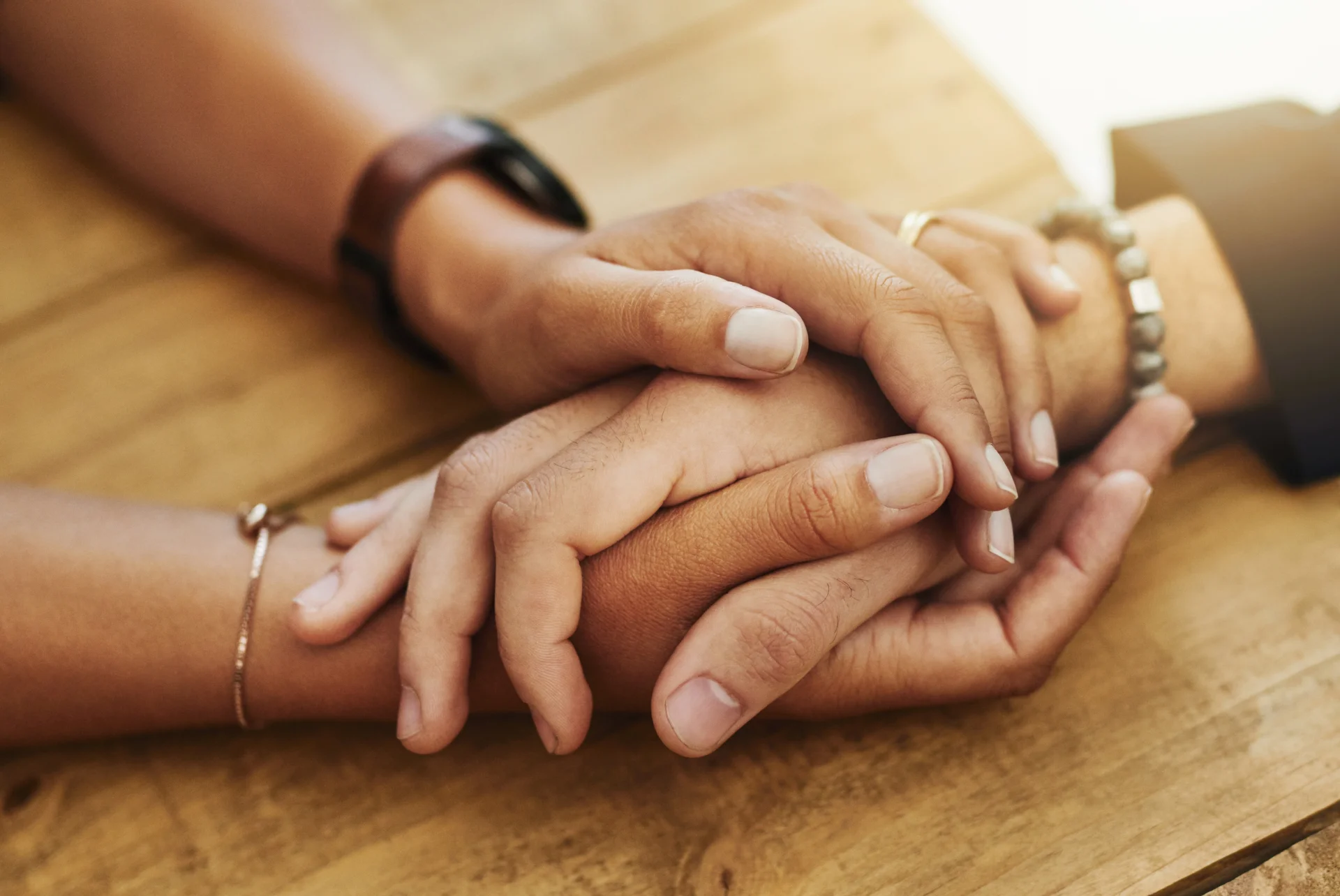 Hands of individuals resting together on a wooden table, symbolizing support and connection in the context of addiction recovery and mental health treatment.