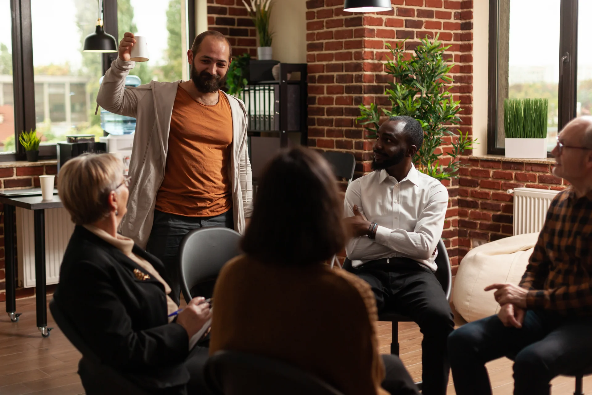 Group therapy session at Hudson Valley Addiction Treatment Center, featuring a diverse group of participants engaged in discussion, with a facilitator holding a coffee cup, in a supportive and structured environment.