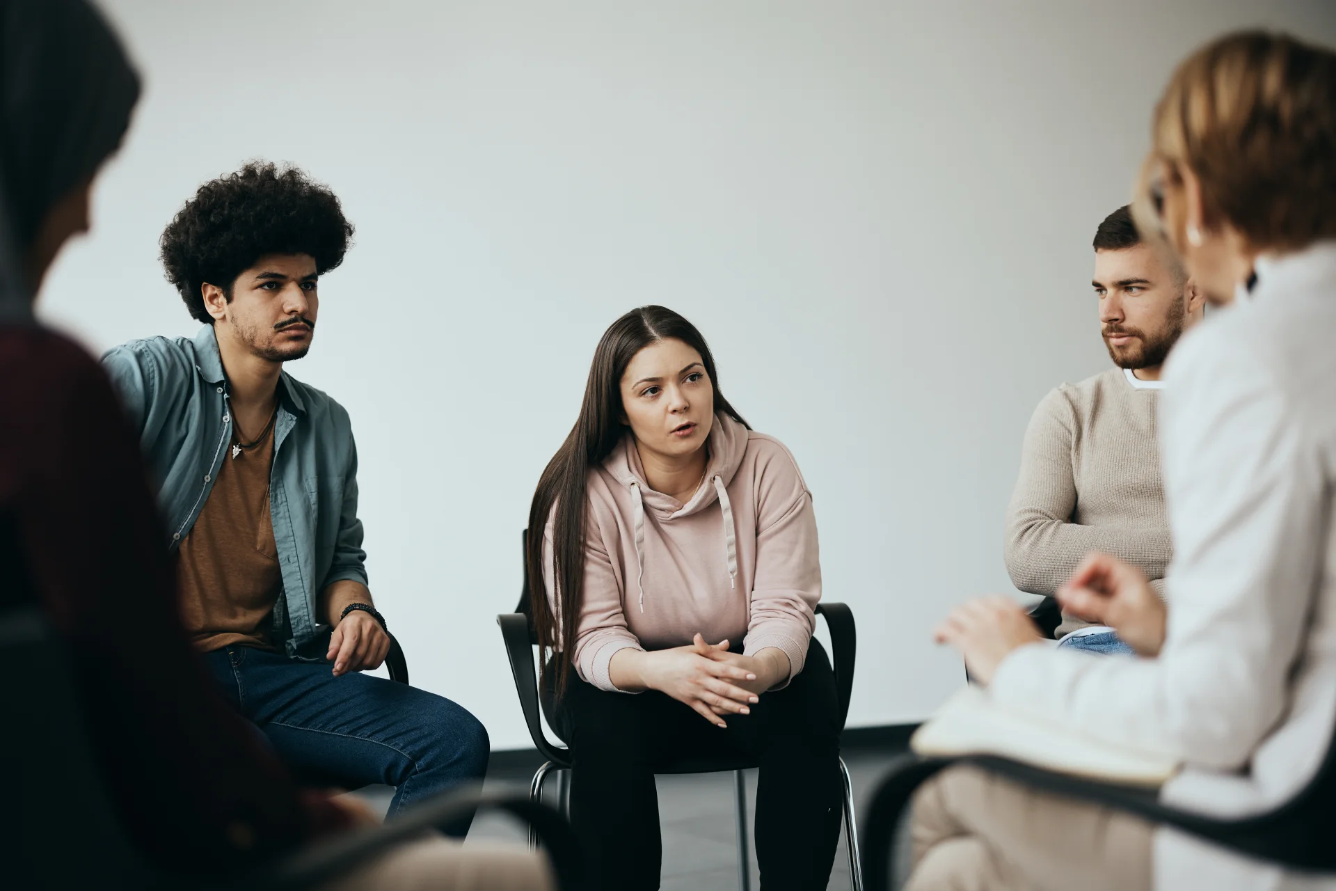 Group therapy session for Adderall addiction, featuring a young woman speaking and attentive participants in a supportive environment.